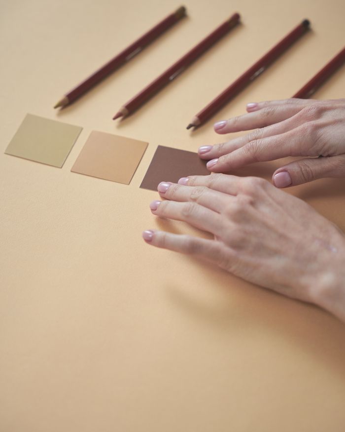 Close-up of hands arranging color swatches and pencils on a yellow background, emphasizing creativity.