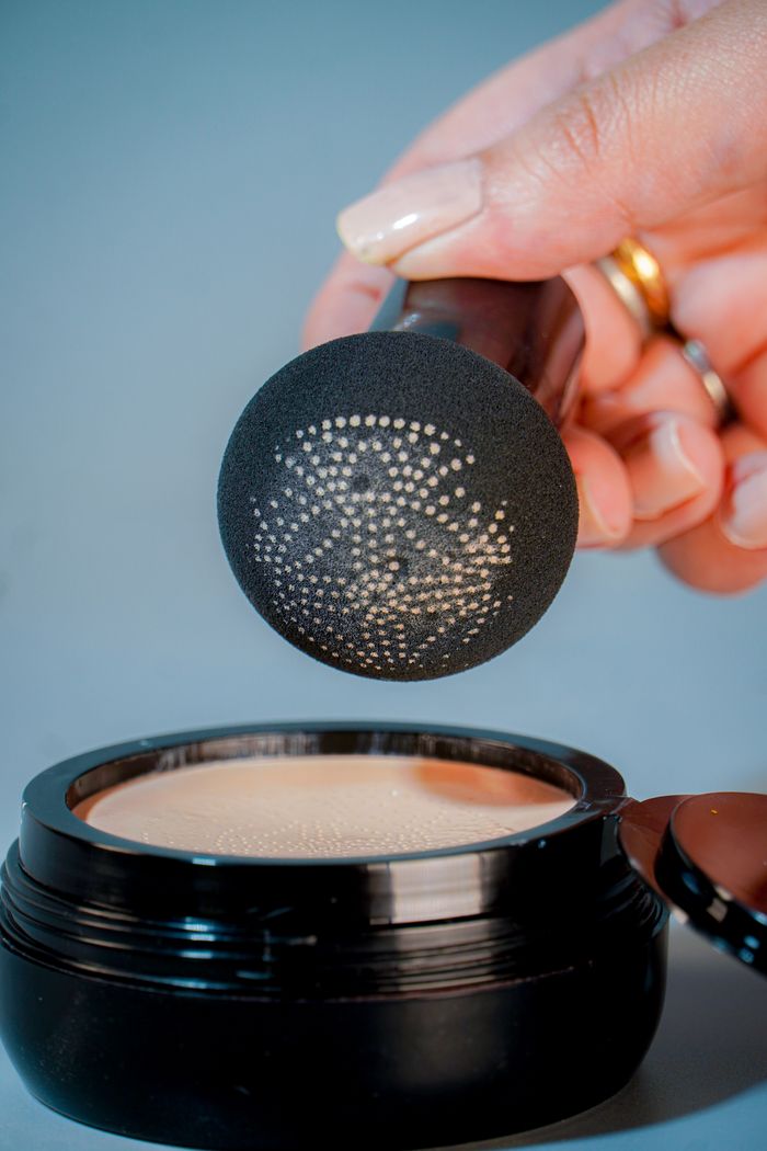Detailed shot of a hand holding a makeup sponge over an open cosmetic container.