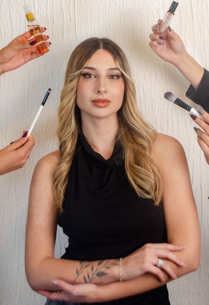 Woman posing with multiple hands holding beauty products and tools around her.