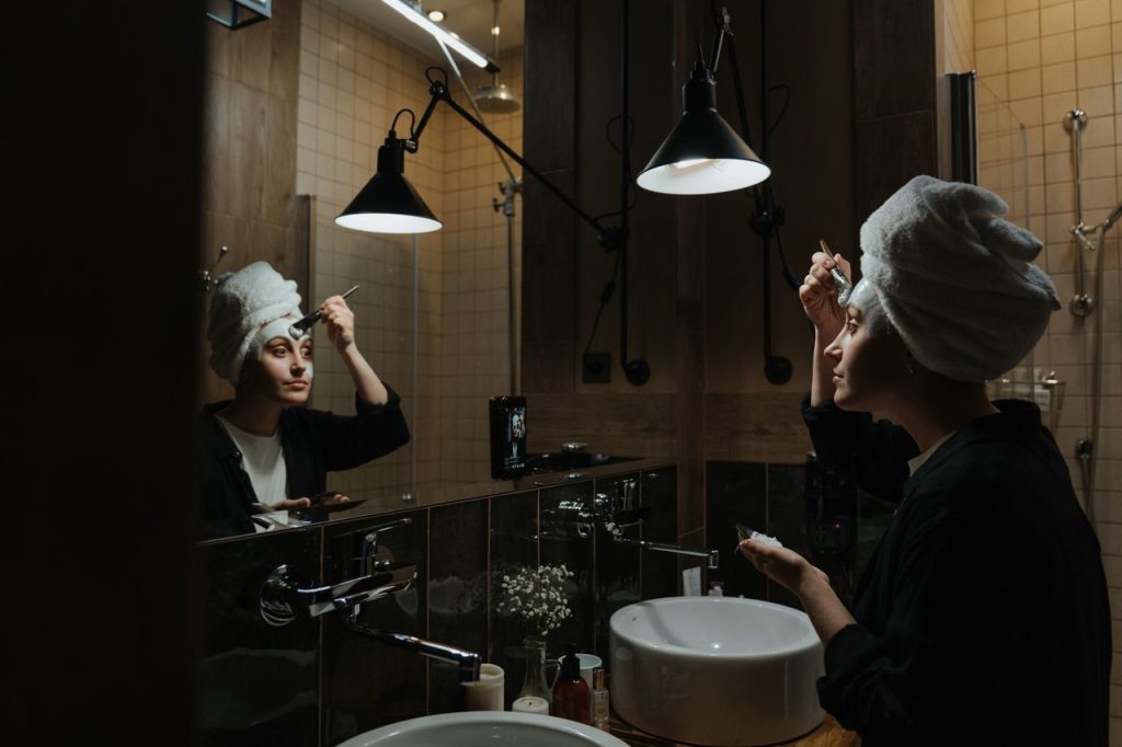 A woman in a towel applies skincare products in a stylish bathroom, focusing on relaxation and freshness.