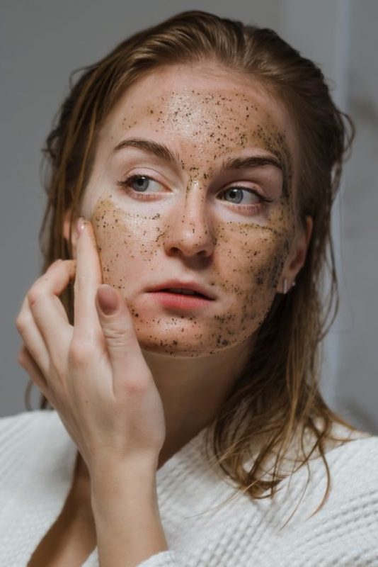 Young woman applying a natural coffee scrub to her face as part of her skincare routine.