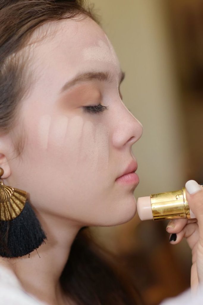 Side view of a woman applying makeup with closed eyes, showcasing technique and elegance.