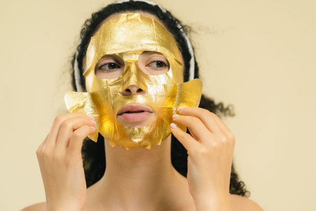 Close-up of woman applying a luxurious gold facial mask as part of skincare routine.